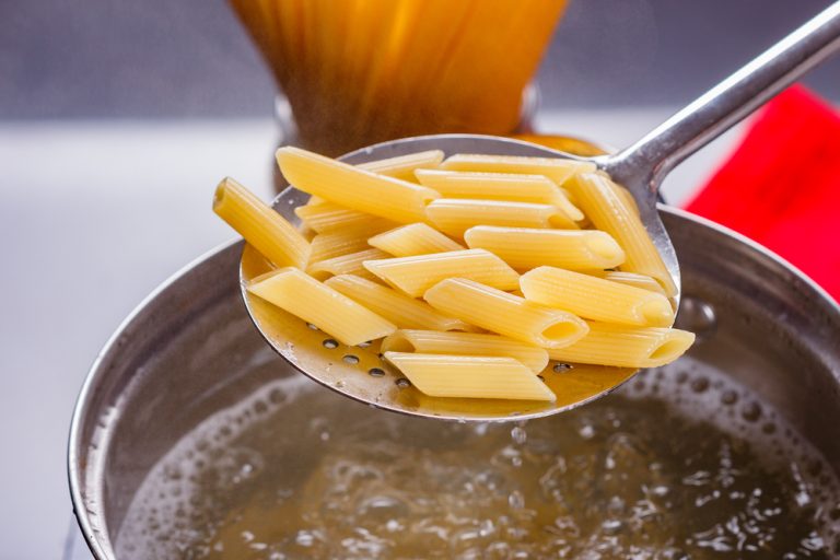 young woman in a gray apron is preparing pasta pesto