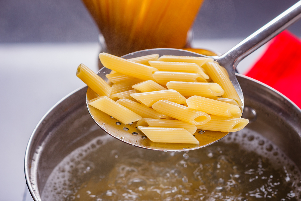young woman in a gray apron is preparing pasta pesto